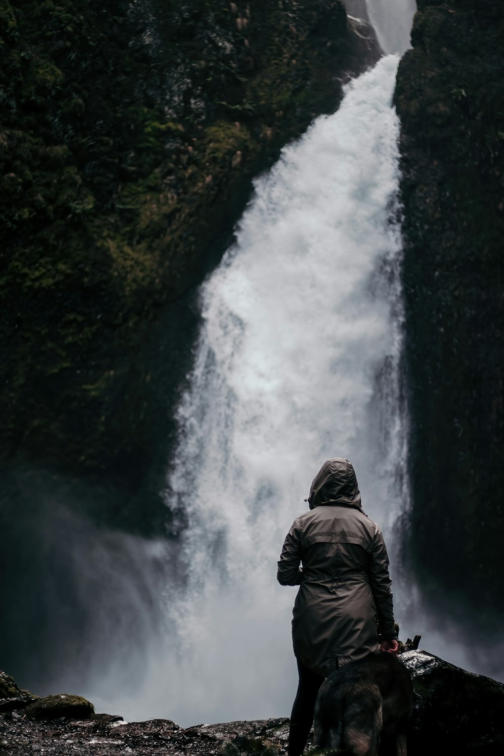 man in black jacket standing in front of waterfalls