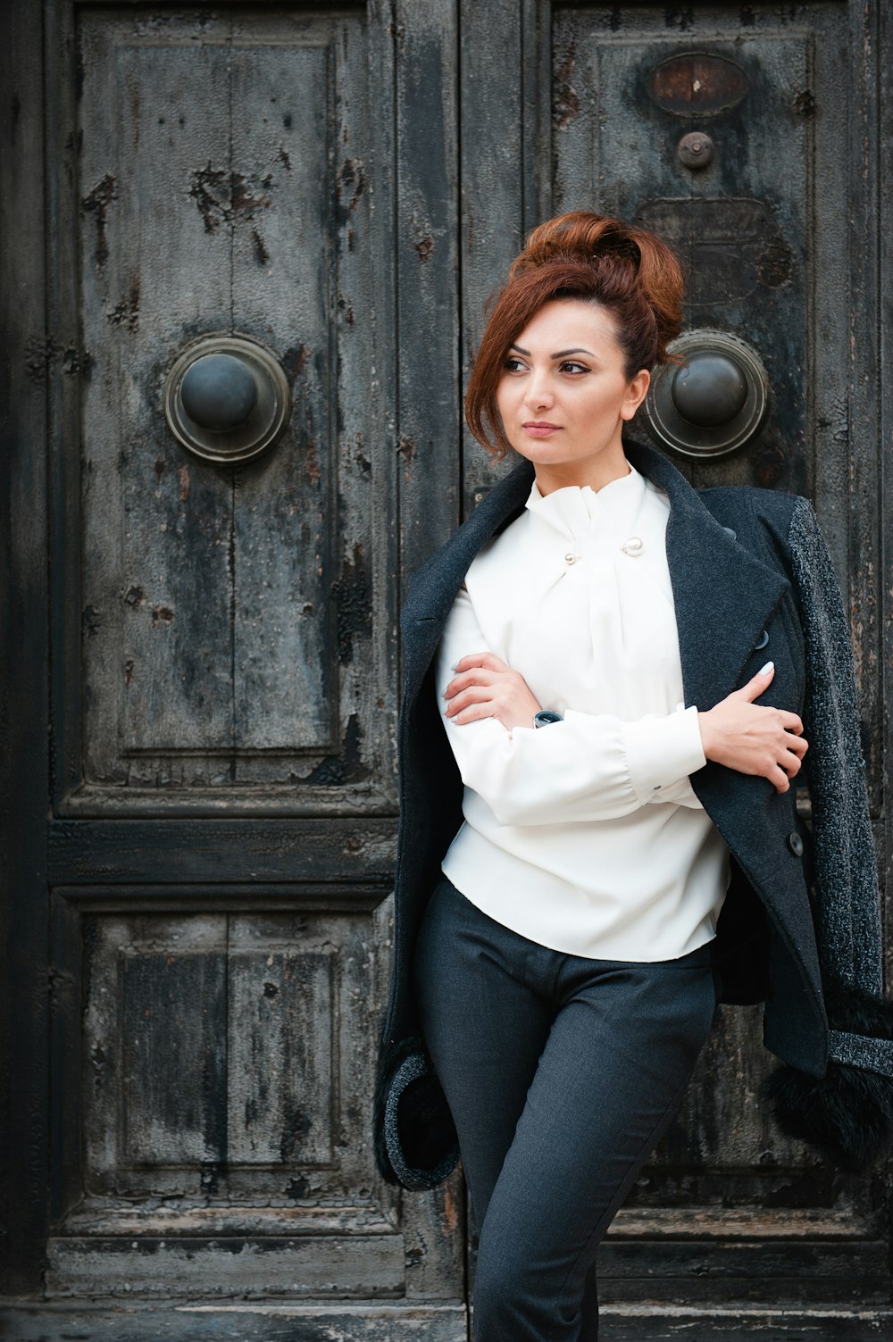 woman in white dress shirt and black pants standing beside black wooden door