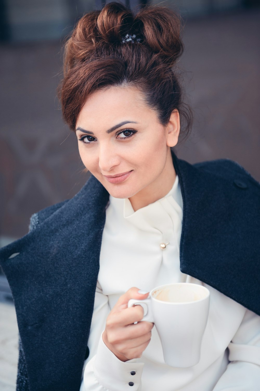 Mujer con blazer negro sosteniendo una taza de cerámica blanca