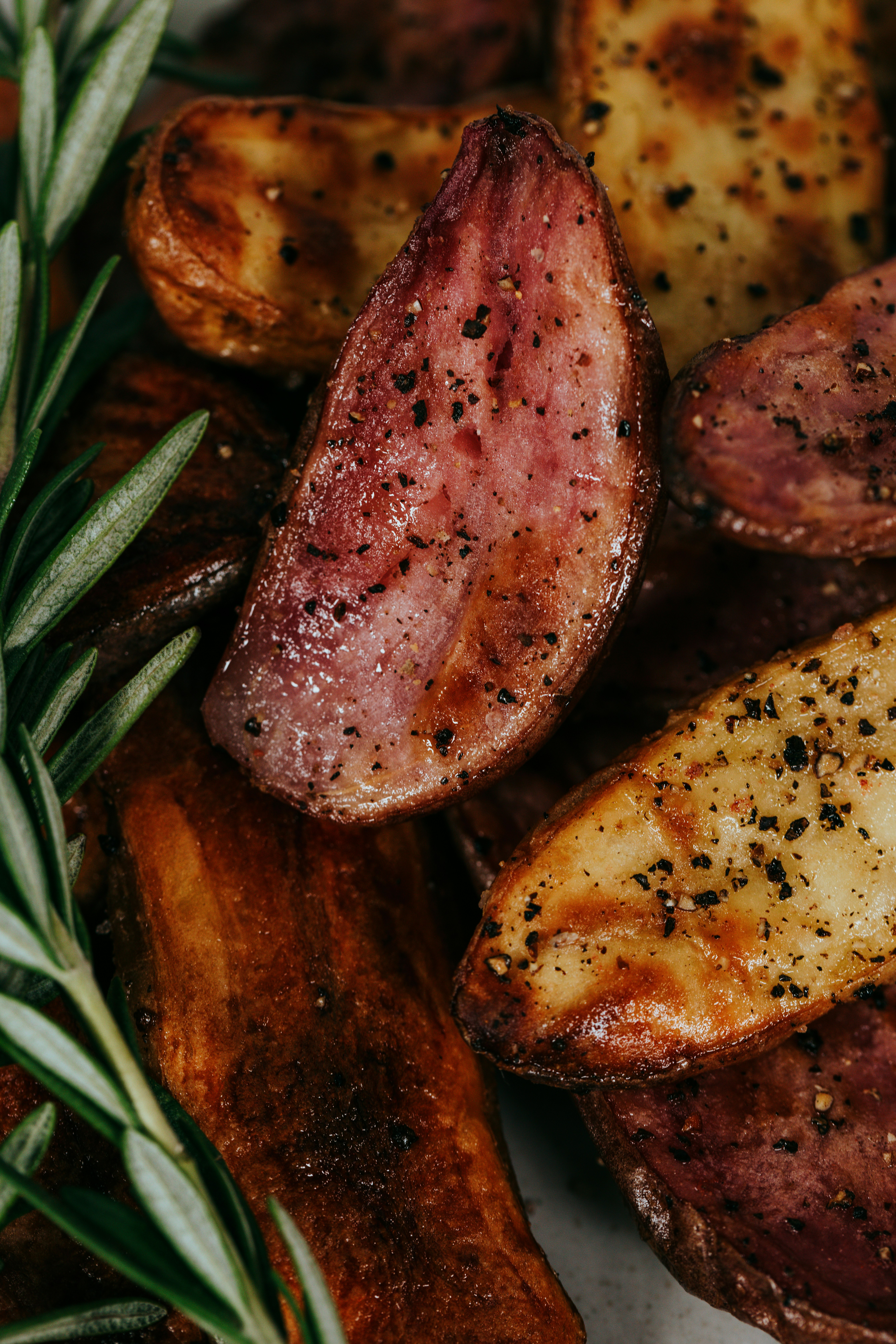 Crispy roasted potato wedges with rosemary sprigs and black pepper seasoning`