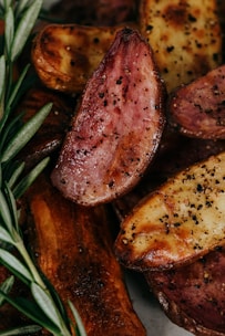 Golden-brown cooked potato wedges spiced with black pepper and garnished with fresh rosemary leaves.