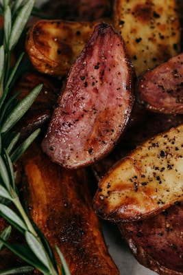 Golden-brown cooked potato wedges spiced with black pepper and garnished with fresh rosemary leaves.