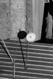 A black and white image depicts a rooftop with a corrugated metal surface. There is a satellite dish mounted on a pole, casting a shadow on a weathered brick wall backdrop. The wall shows signs of wear with visible cracks.