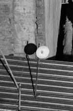 A black and white image depicts a rooftop with a corrugated metal surface. There is a satellite dish mounted on a pole, casting a shadow on a weathered brick wall backdrop. The wall shows signs of wear with visible cracks.