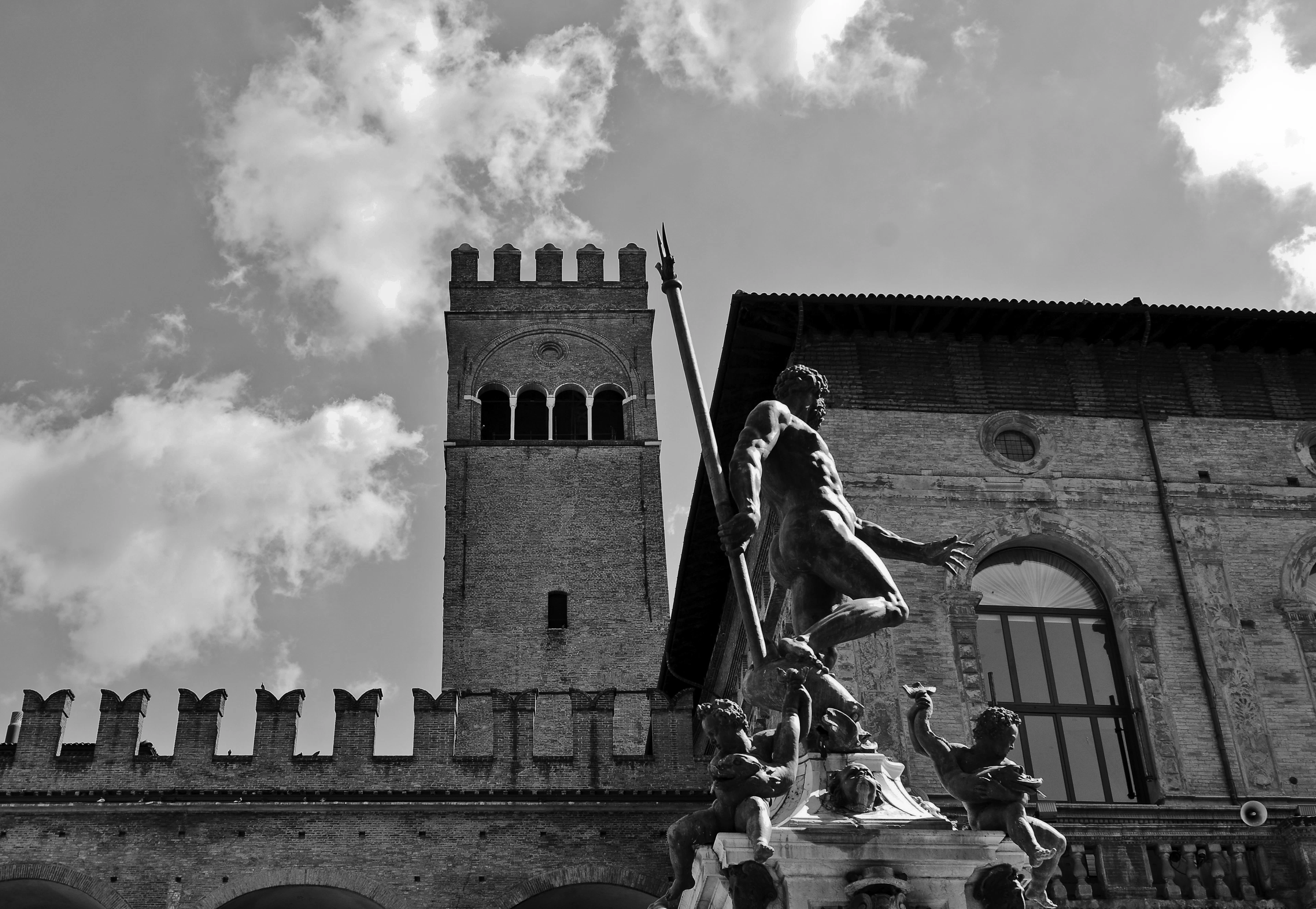 Black-and-white view of the Neptune Fountain statue against a crenellated medieval tower and dramatic clouds.