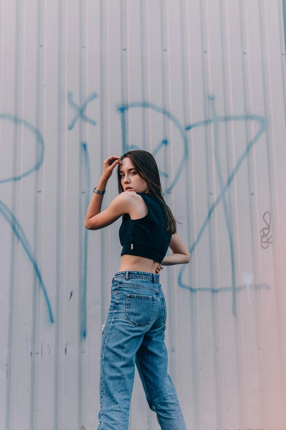 woman in black crop top and blue denim jeans standing beside white wall during daytime