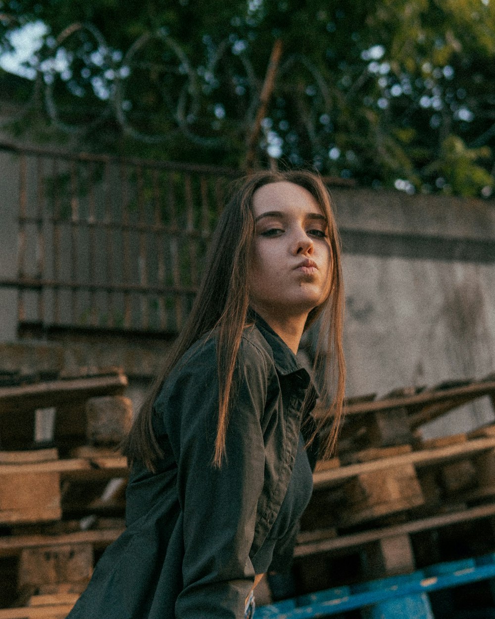 woman in black leather jacket standing near brown wooden fence during daytime