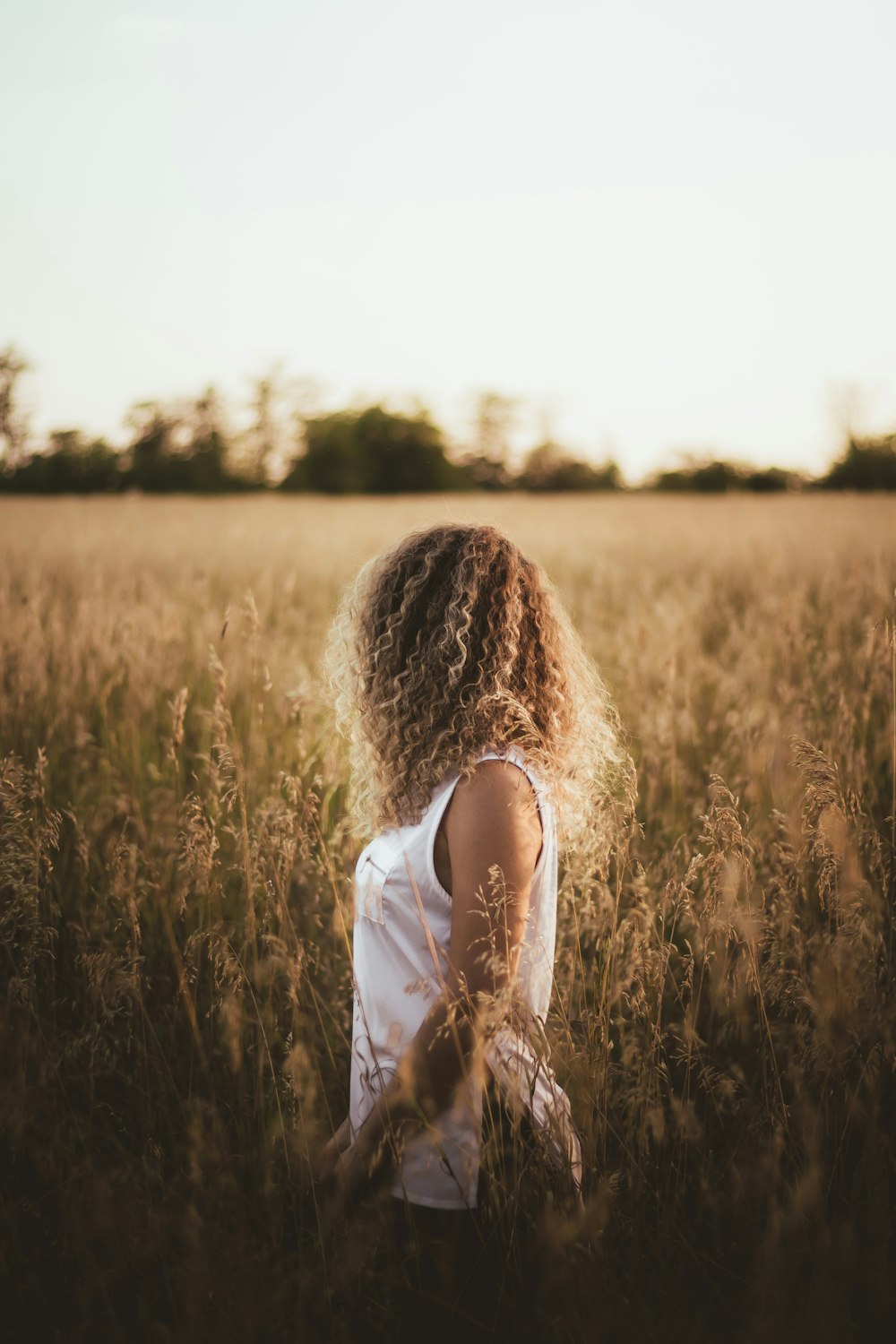 woman in white tank top standing on brown grass field during daytime