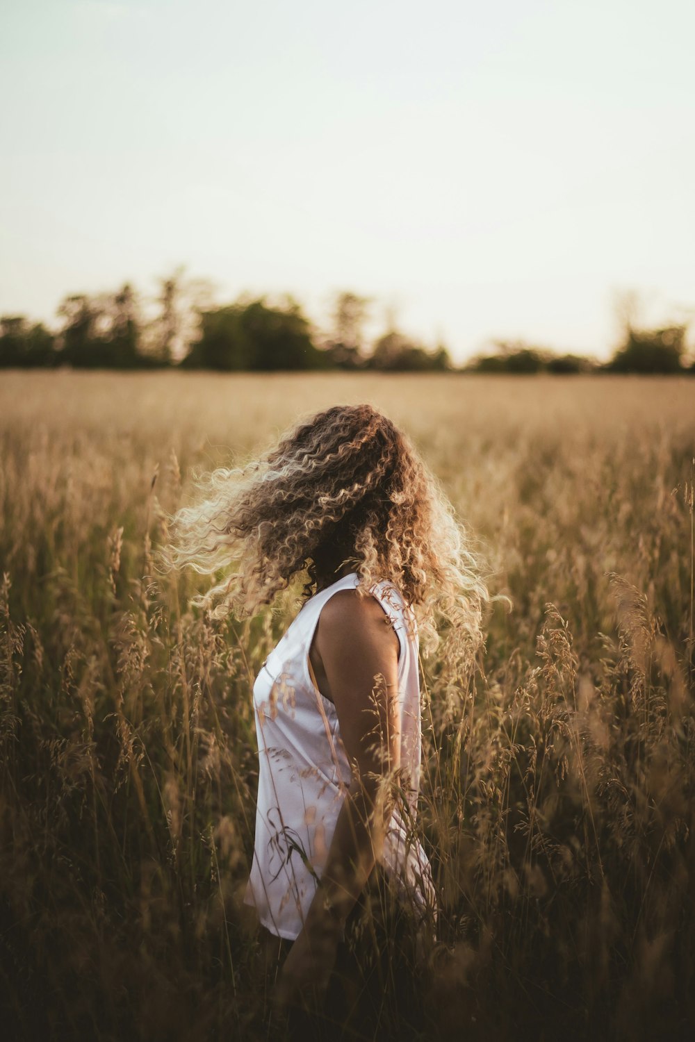 woman in white tank top standing on brown grass field during daytime