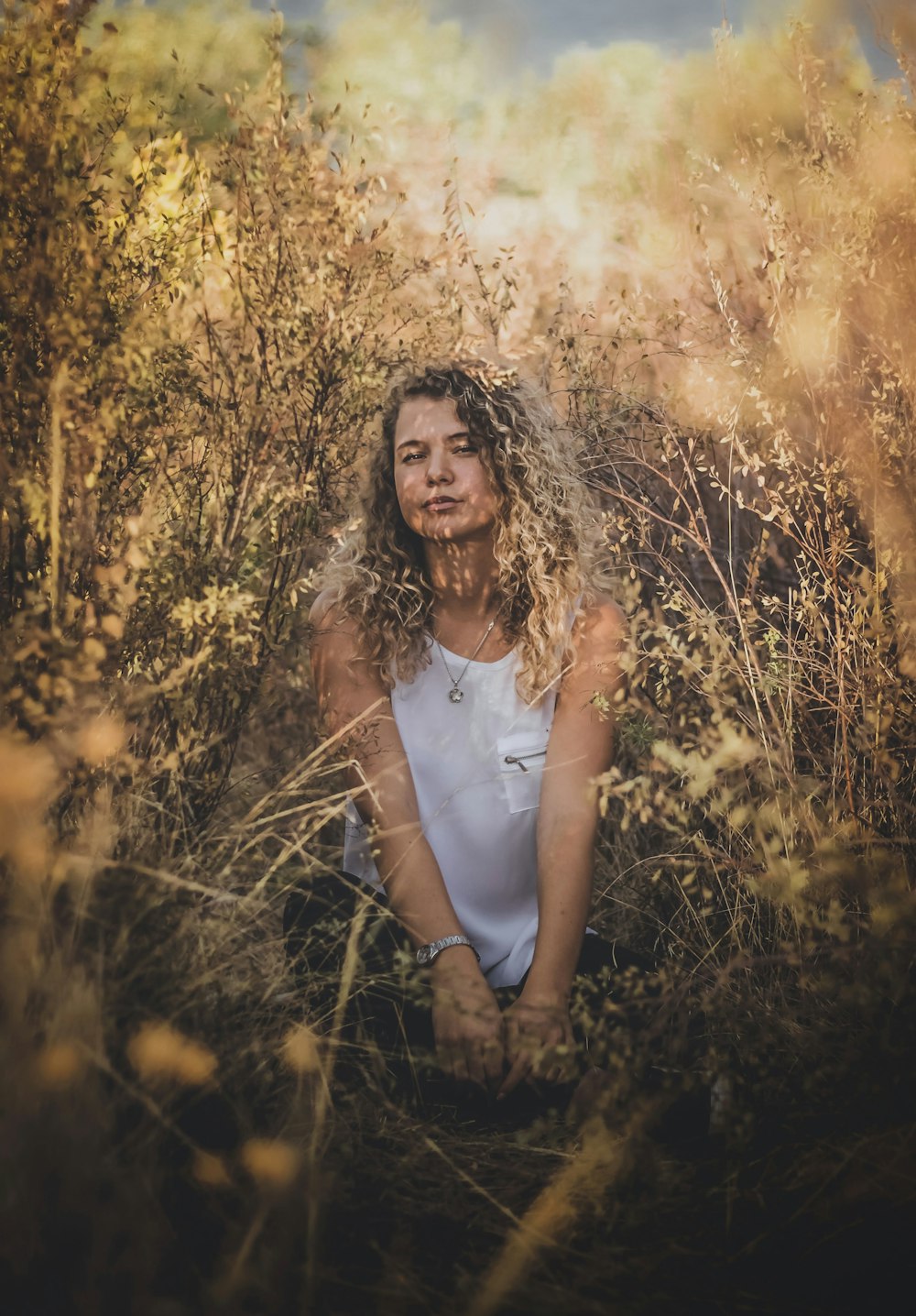 femme en débardeur blanc assise sur le champ d’herbe brune