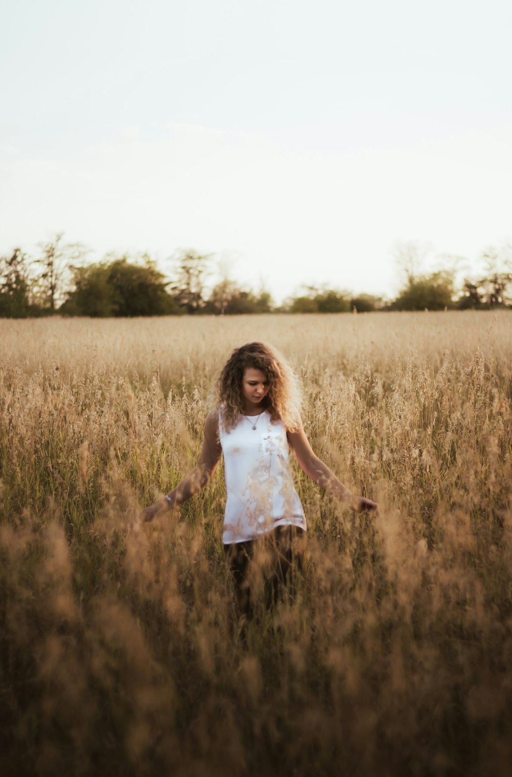 woman in white tank top standing on brown grass field during daytime