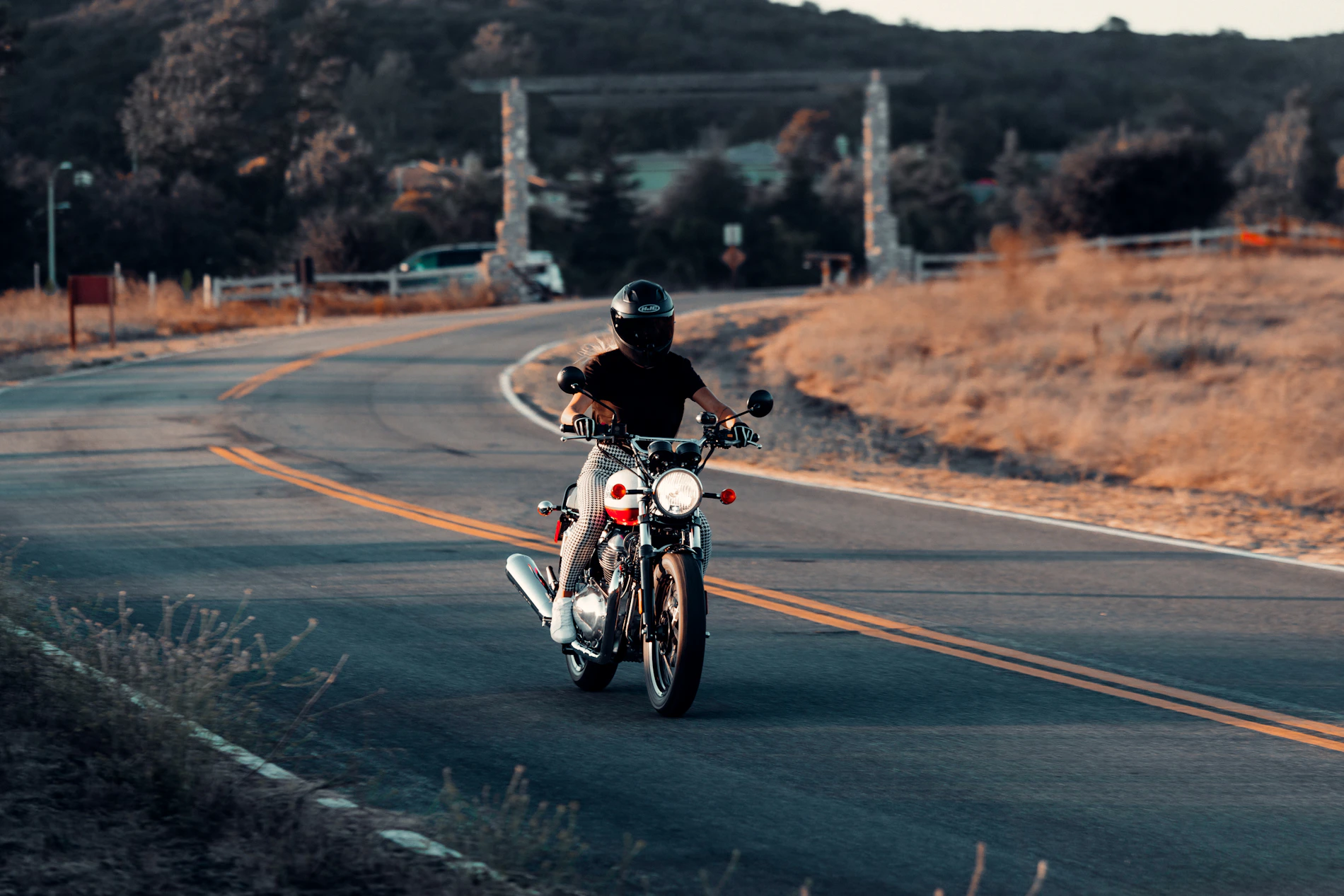 Motorcycle rider in dark riding gear on a cafe racer during a road ride