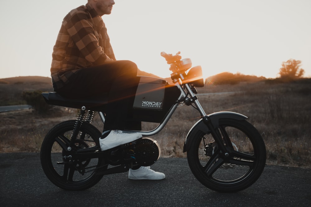 homme en chemise à carreaux marron et blanc conduisant une moto noire au coucher du soleil