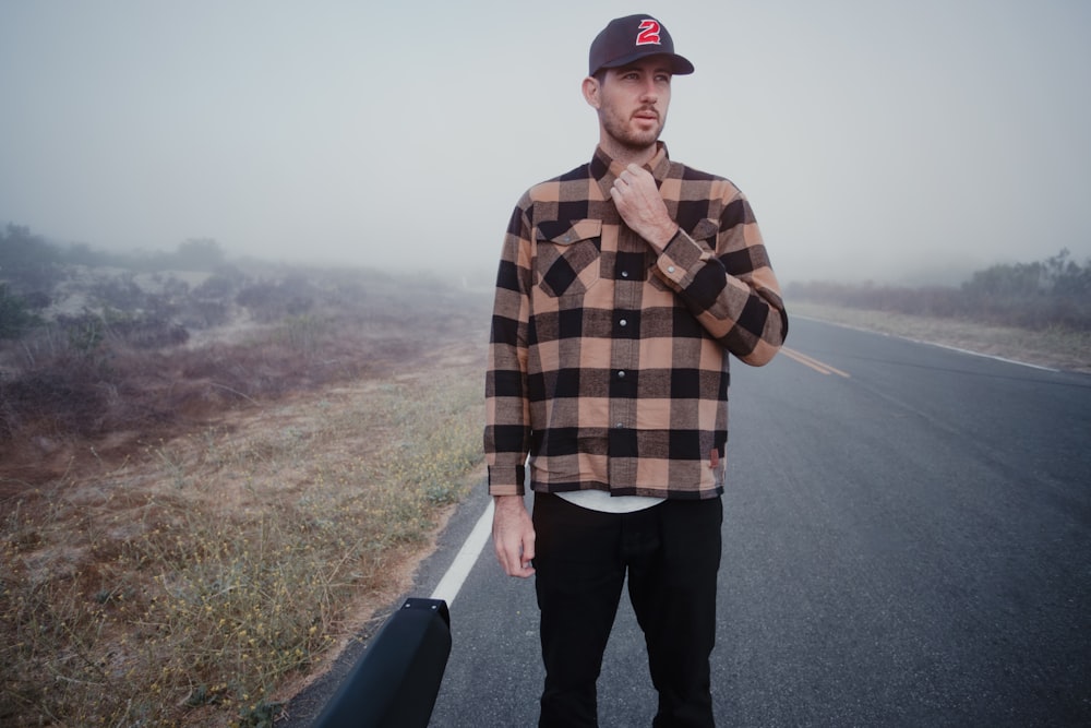 man in brown and black plaid dress shirt and black pants standing on road during daytime