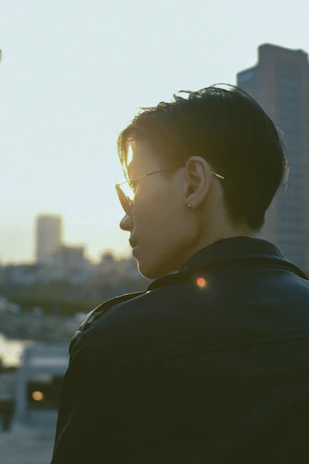 A model wearing classic aviator sunglasses against a city skyline at dusk.