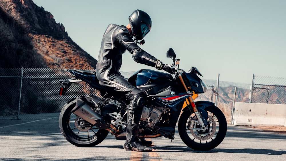 man in black leather jacket riding on black and orange sports bike