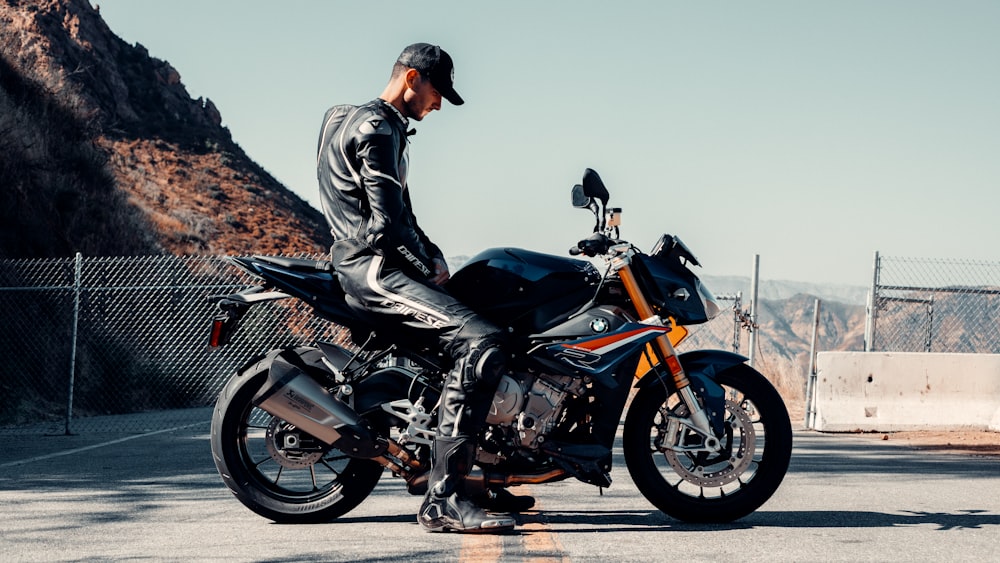 man in black leather jacket riding on black and orange sports bike