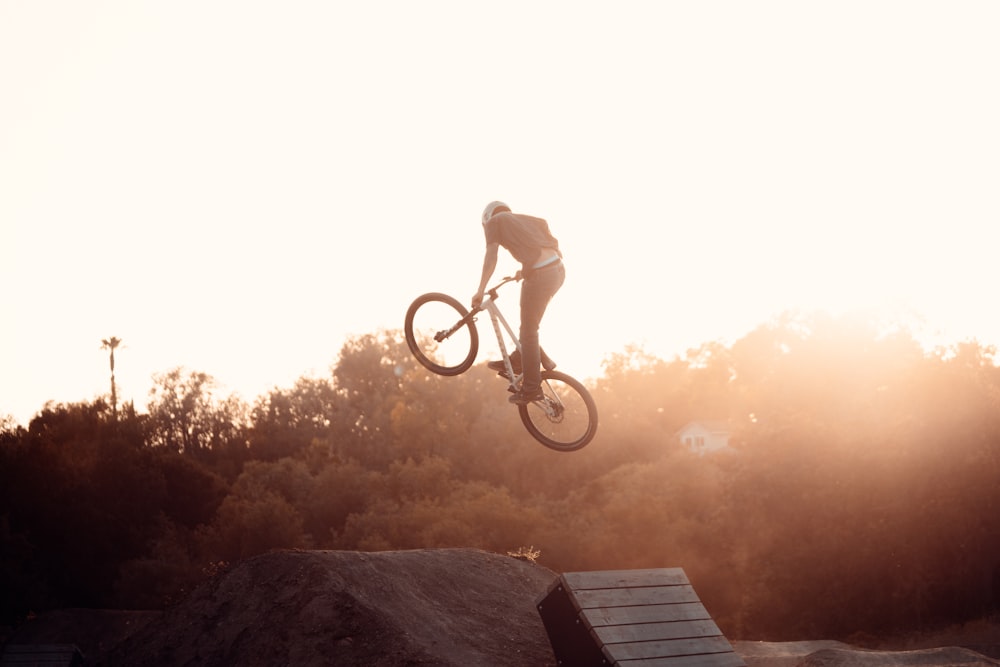 silhueta do homem que monta a bicicleta durante o pôr do sol