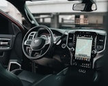 The interior of a modern vehicle featuring a steering wheel with multiple controls and a large touchscreen display showing a navigation map. The dashboard is sleek with black and metallic accents, integrating various buttons and vents.
