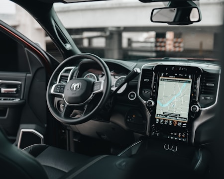 The interior of a modern vehicle featuring a steering wheel with multiple controls and a large touchscreen display showing a navigation map. The dashboard is sleek with black and metallic accents, integrating various buttons and vents.