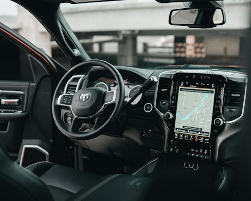 The interior of a modern vehicle featuring a steering wheel with multiple controls and a large touchscreen display showing a navigation map. The dashboard is sleek with black and metallic accents, integrating various buttons and vents.