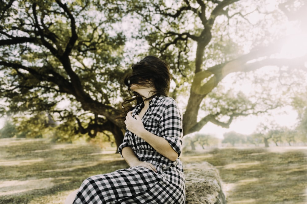 woman in black and white plaid dress sitting on rock during daytime