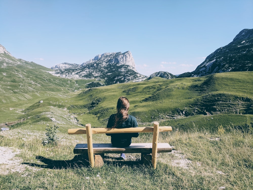 woman sitting on brown wooden bench on green grass field during daytime