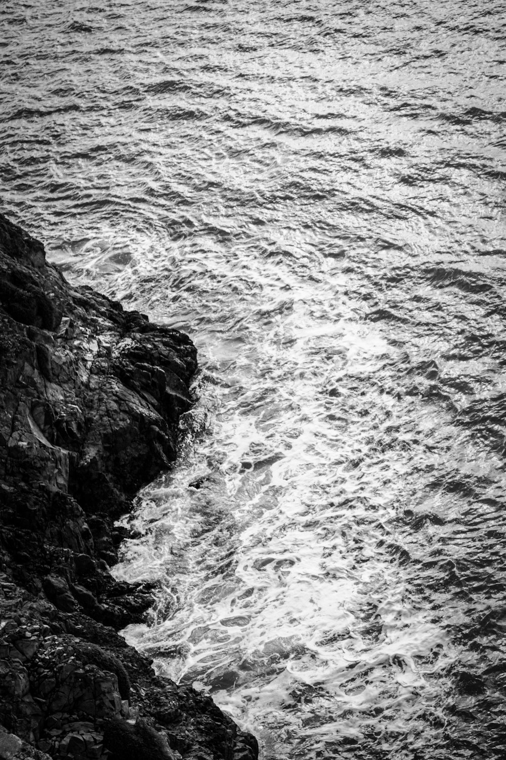 grayscale photo of ocean waves crashing on rock