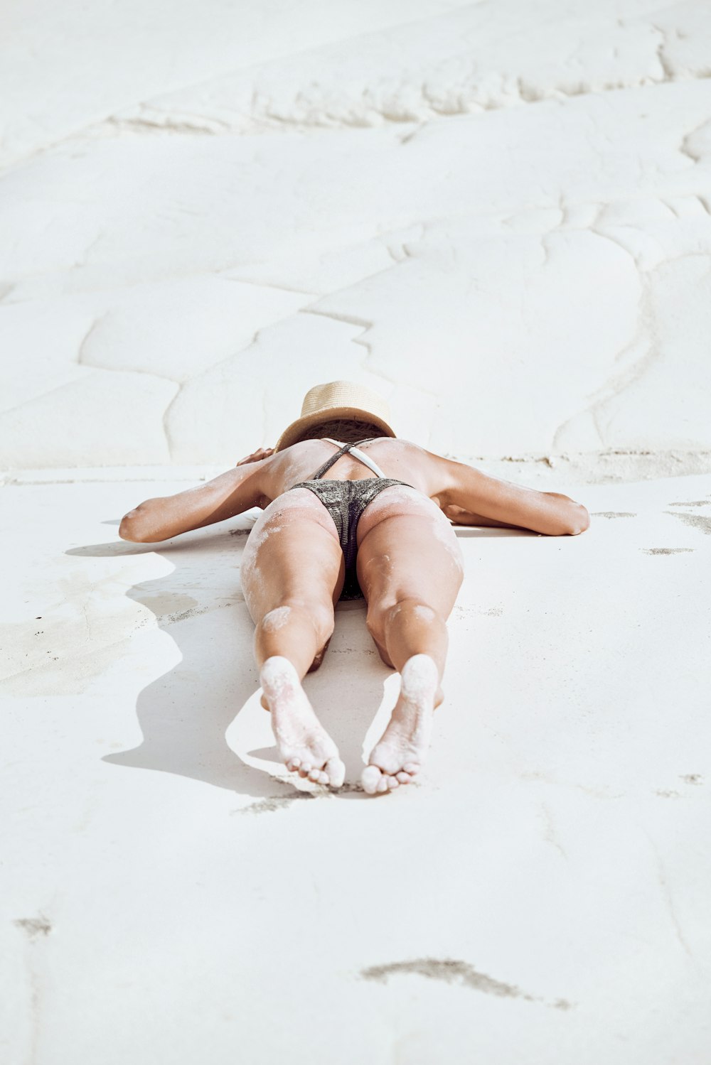 woman in black bikini lying on white sand during daytime