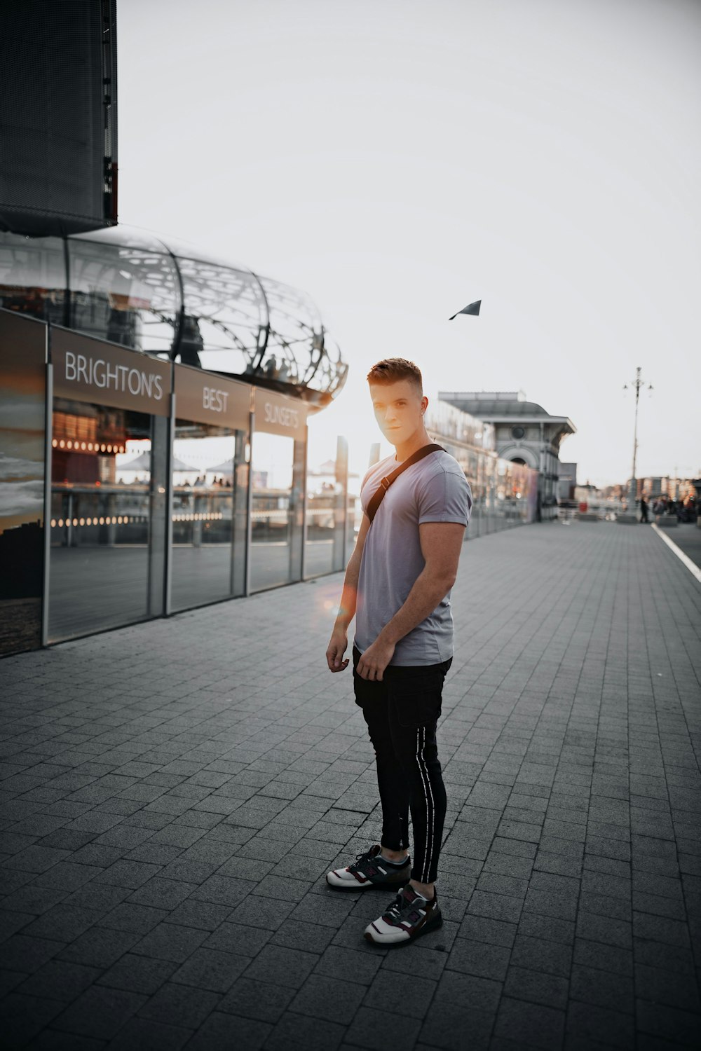man in white crew neck t-shirt and black pants standing on sidewalk during daytime