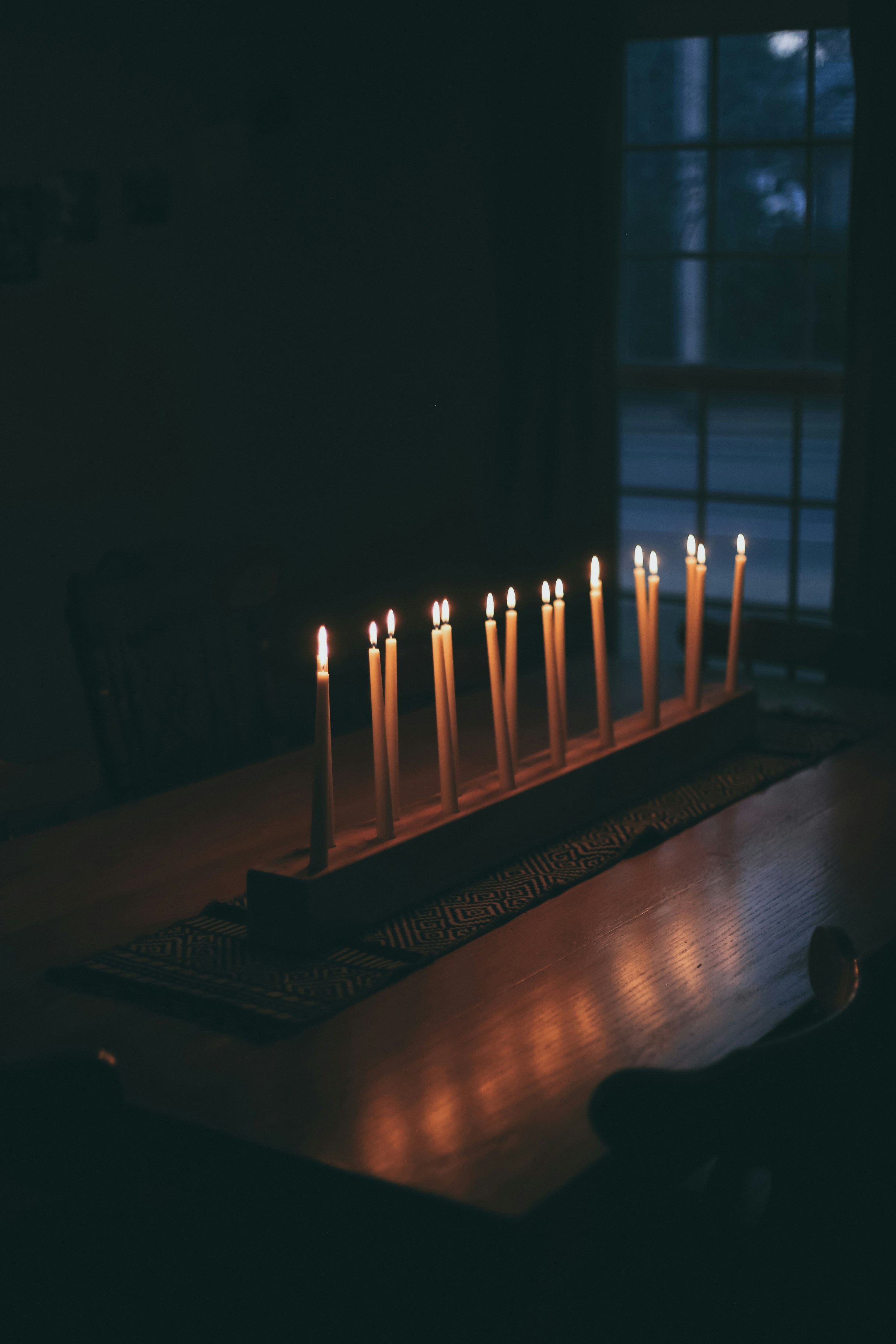 Lit candles stand in a wooden holder on a table.