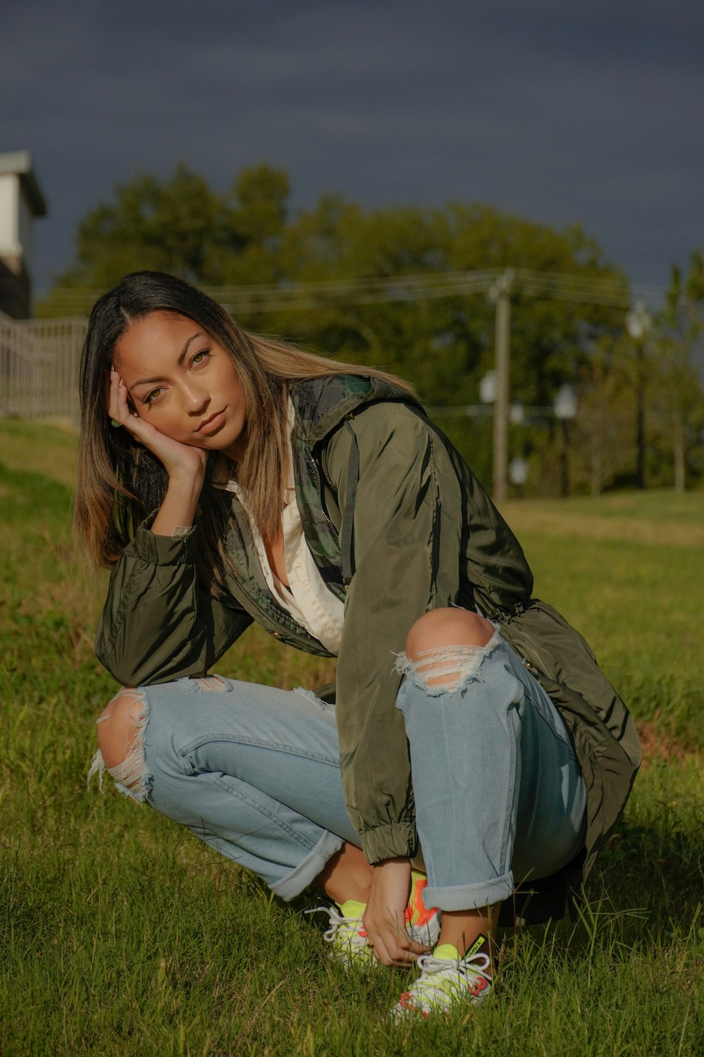woman in green jacket and blue denim jeans sitting on green grass field during daytime