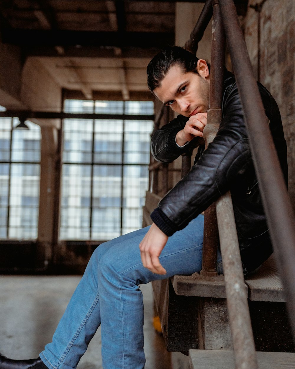 man in black leather jacket and blue denim jeans sitting on brown wooden  bench photo – Free Clothing Image on Unsplash