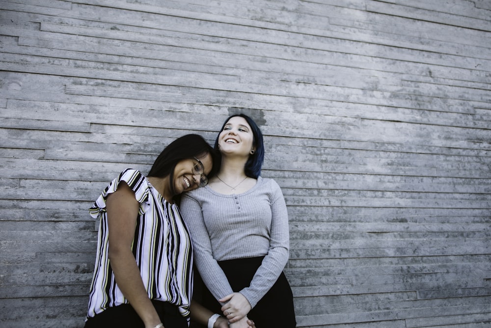 2 women standing beside gray wooden wall