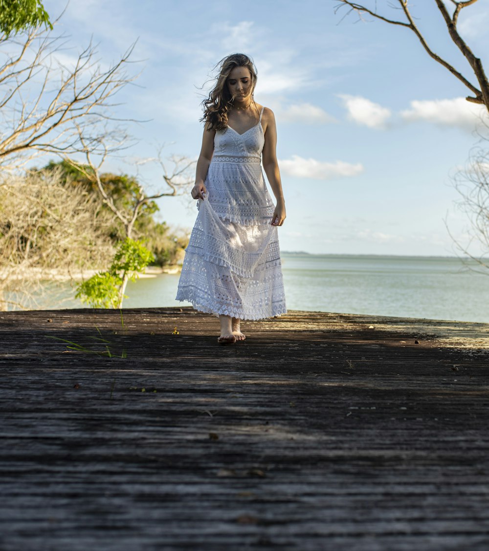 woman in white sleeveless dress standing on wooden dock during daytime
