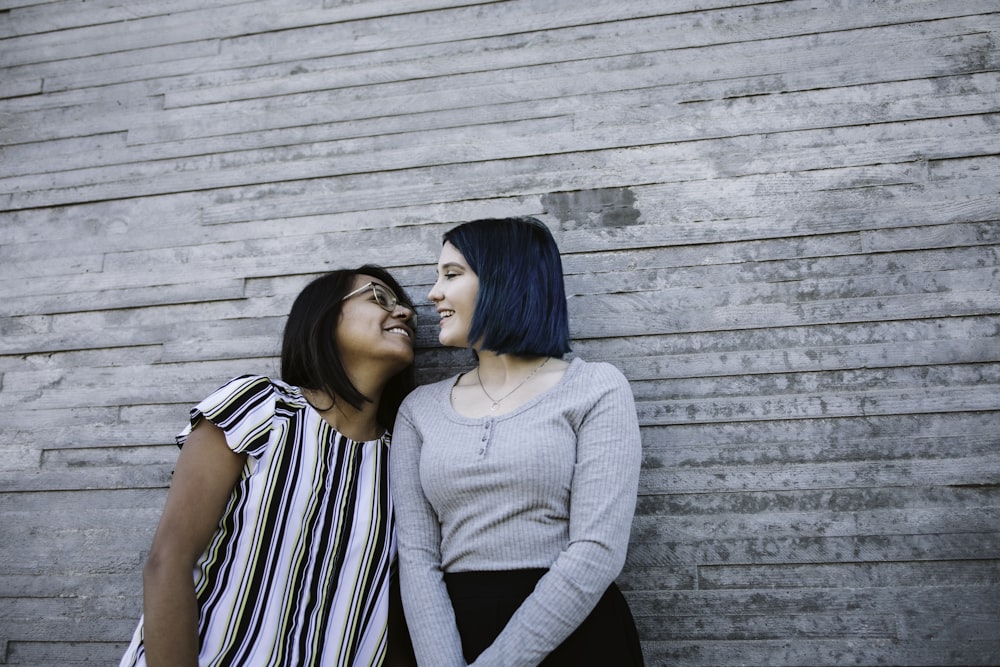 2 women standing beside gray wooden wall