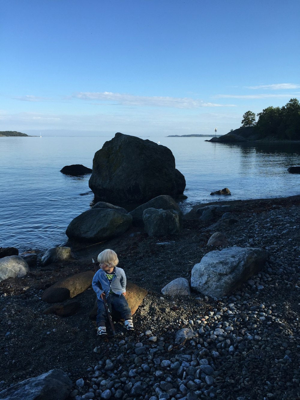 woman in blue jacket sitting on rock near body of water during daytime