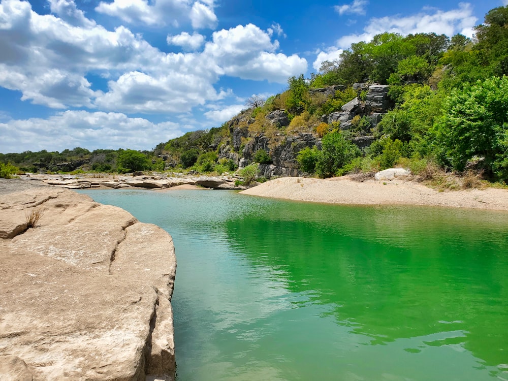 green body of water near brown rocky mountain under blue and white sunny cloudy sky during