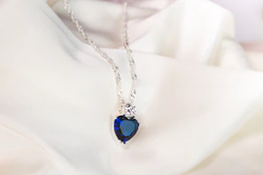 Close-up of a delicate aquamarine crystal pendant glowing softly against a pastel blue background