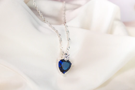 A close-up of a delicate silver necklace with a small gemstone pendant resting on a soft fabric background.