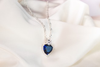 Close-up of a handcrafted silver necklace with a deep blue sapphire pendant against a black background