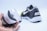A pair of black and white athletic shoes are displayed. One shoe is held in a hand showing the sole, which has a textured, waffle-like pattern. The other shoe rests on its side, highlighting the brand logo on the heel.