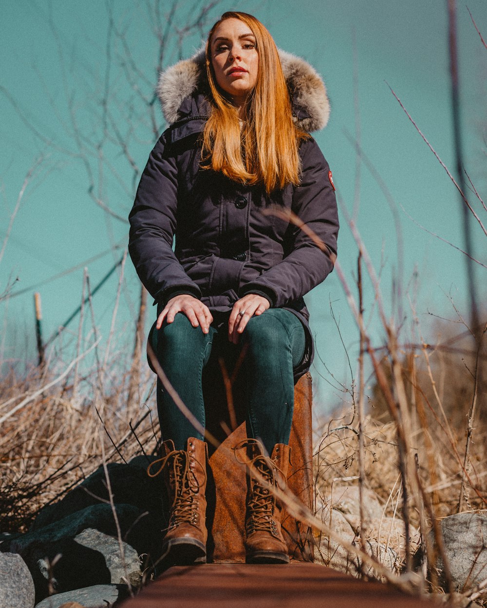 woman in black jacket and blue denim jeans sitting on brown rock