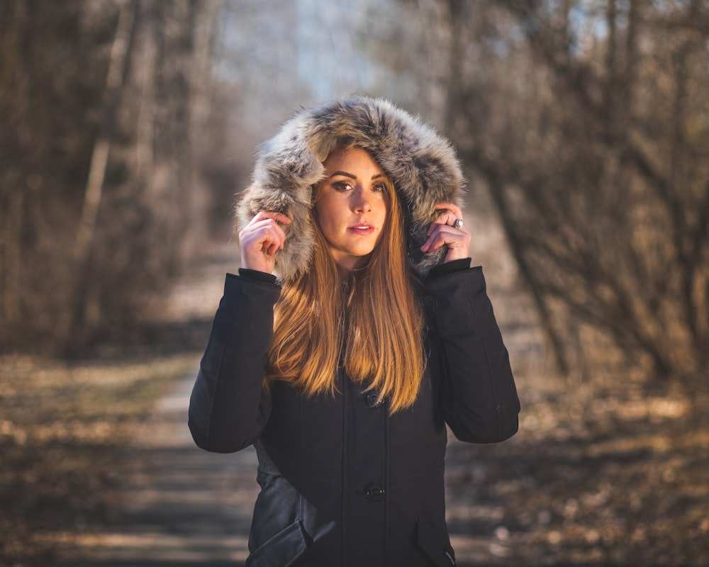 woman in black coat standing near trees during daytime