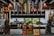 A bar setup with a variety of beer taps hanging from a black metal pipe and several liquor bottles placed on the counter. Two bottles of Bulleit whiskey are prominently displayed in the center. The background features bar stools and soft lighting from hanging pendant lamps.