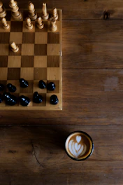A stylish chessboard with a steaming cup of cocoa beside it, set against a backdrop of deep browns and black.