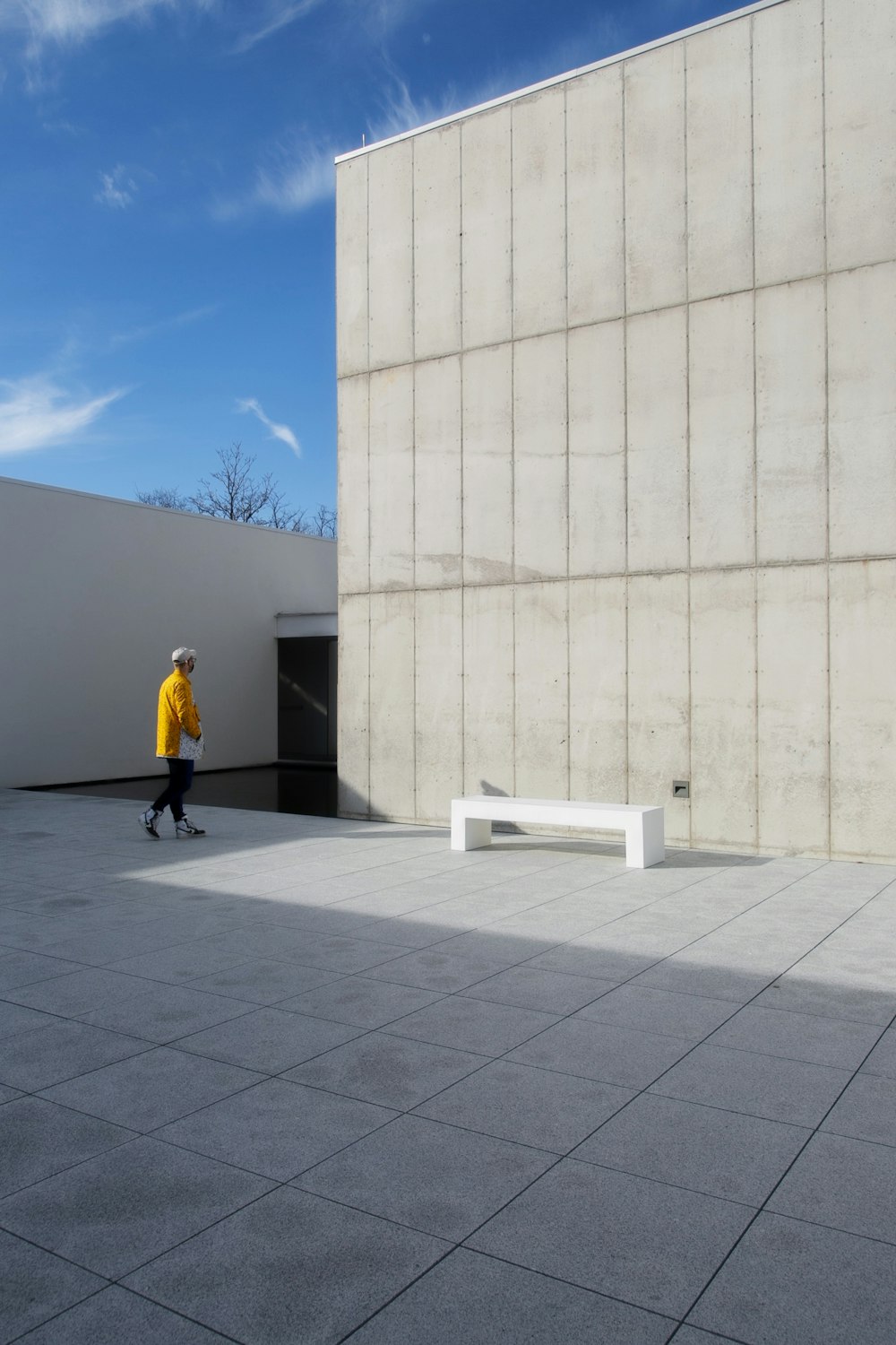 man in yellow jacket and black pants walking on gray concrete floor during daytime