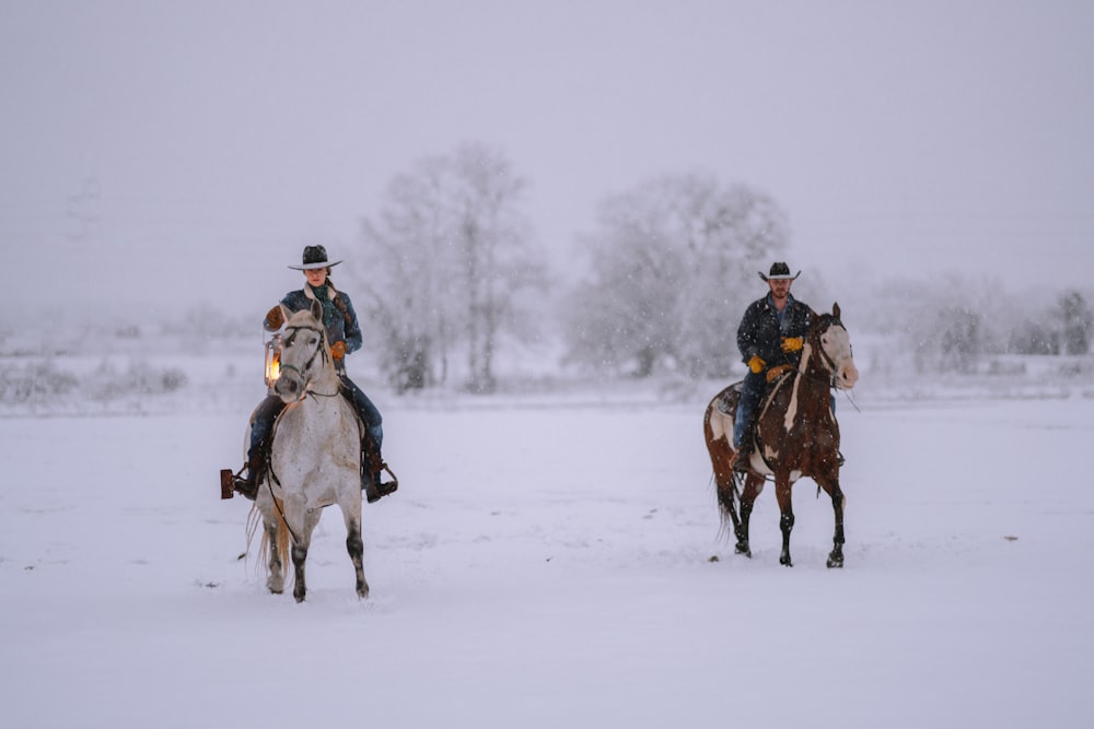 2 men riding horses on snow covered field during daytime