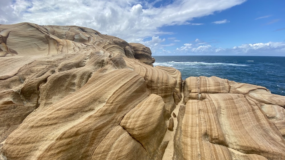 a rocky cliff next to the ocean under a blue sky