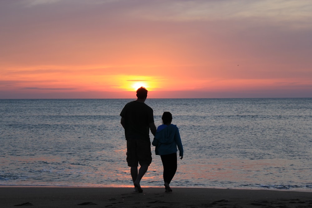 hombre y mujer de pie en la playa durante la puesta del sol